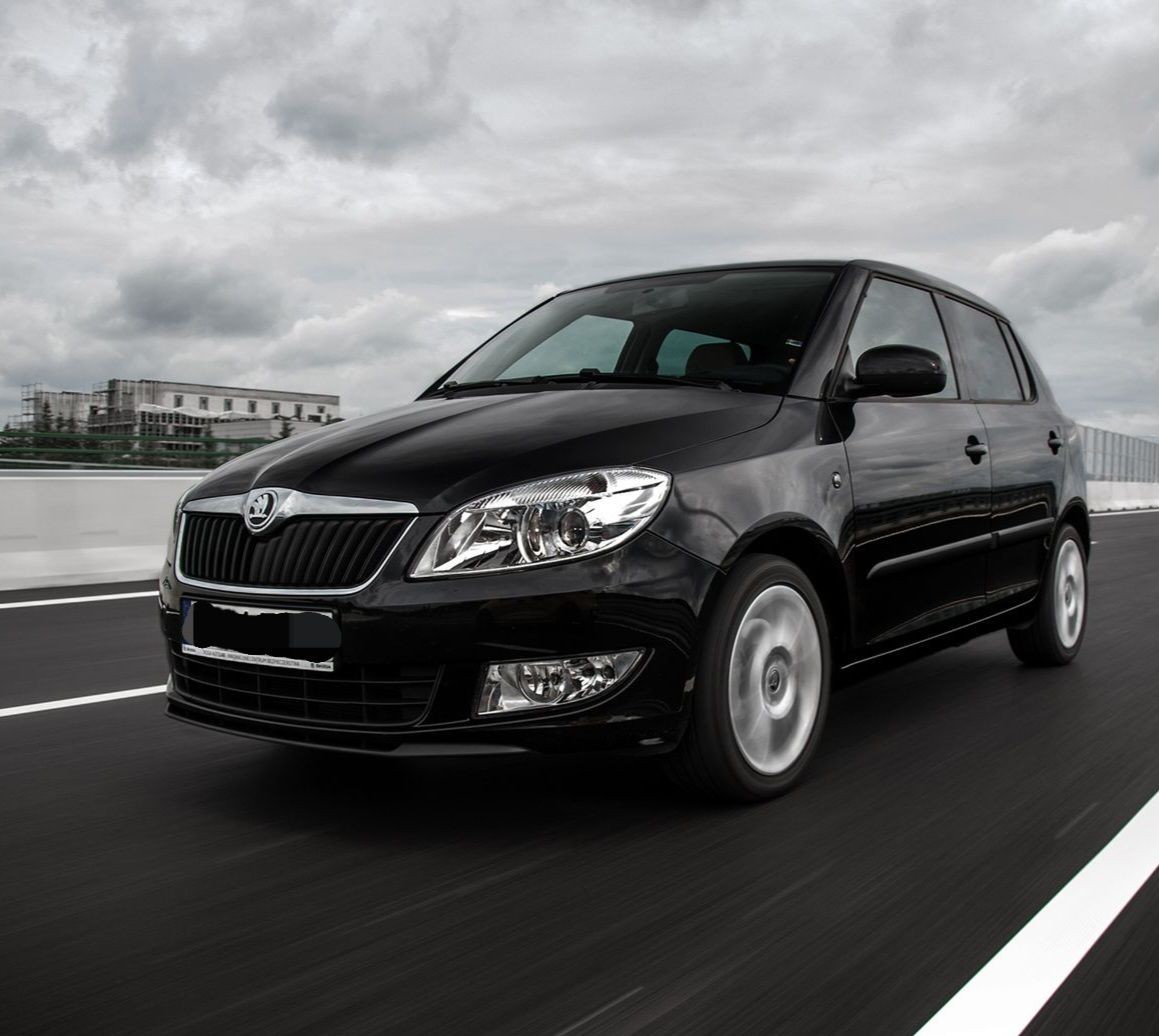 A black car driving on a highway with overcast skies in the background.