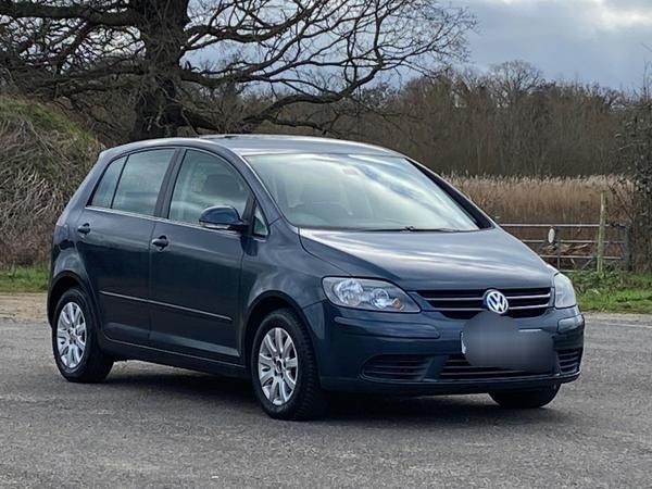 Blue Volkswagen car parked outdoors with trees and a fence in the background on a cloudy day.